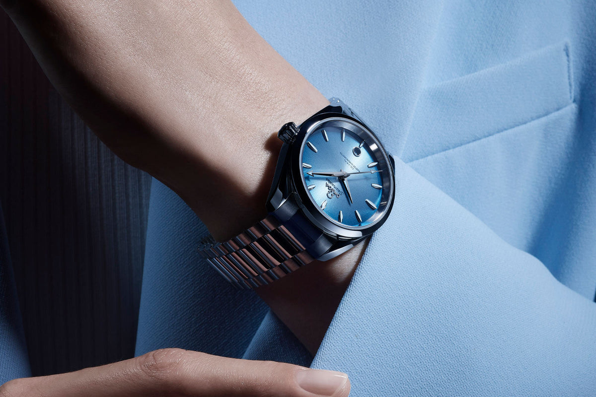 Omega Seamaster Aqua Terra 150M Co-Axial Master Chronometer 38mm with a summer blue sunray dial on a steel bracelet, worn against a pale blue coat