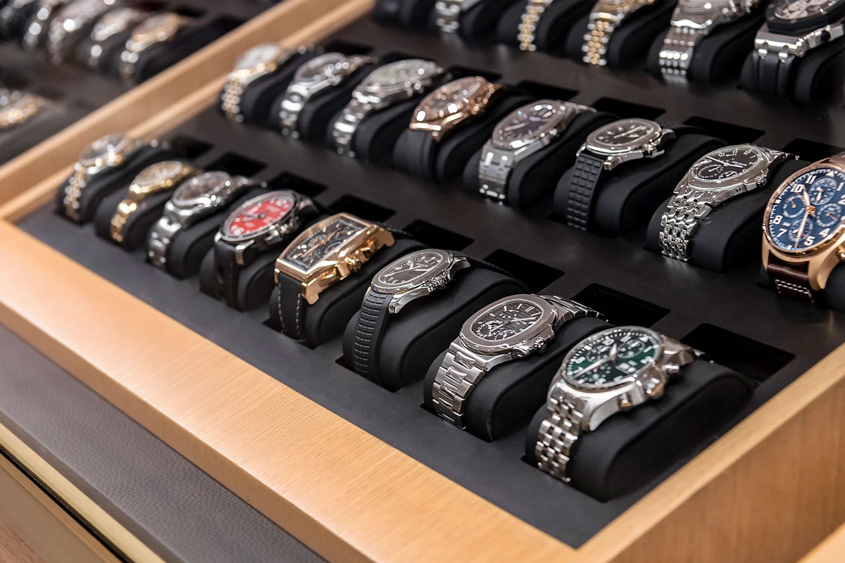 A dealer display tray of pre-owned luxury watches resting on black cushions, including steel sports chronographs and dive watches, representing secondary market inventory