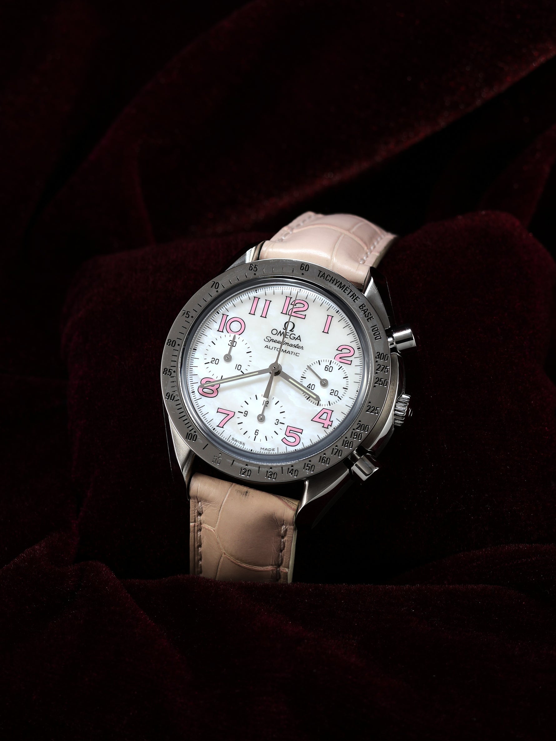 Omega Speedmaster Automatic Chronograph 38mm Ref. 3834.74.34 – right side view, white mother-of-pearl dial, pink leather strap, dark background