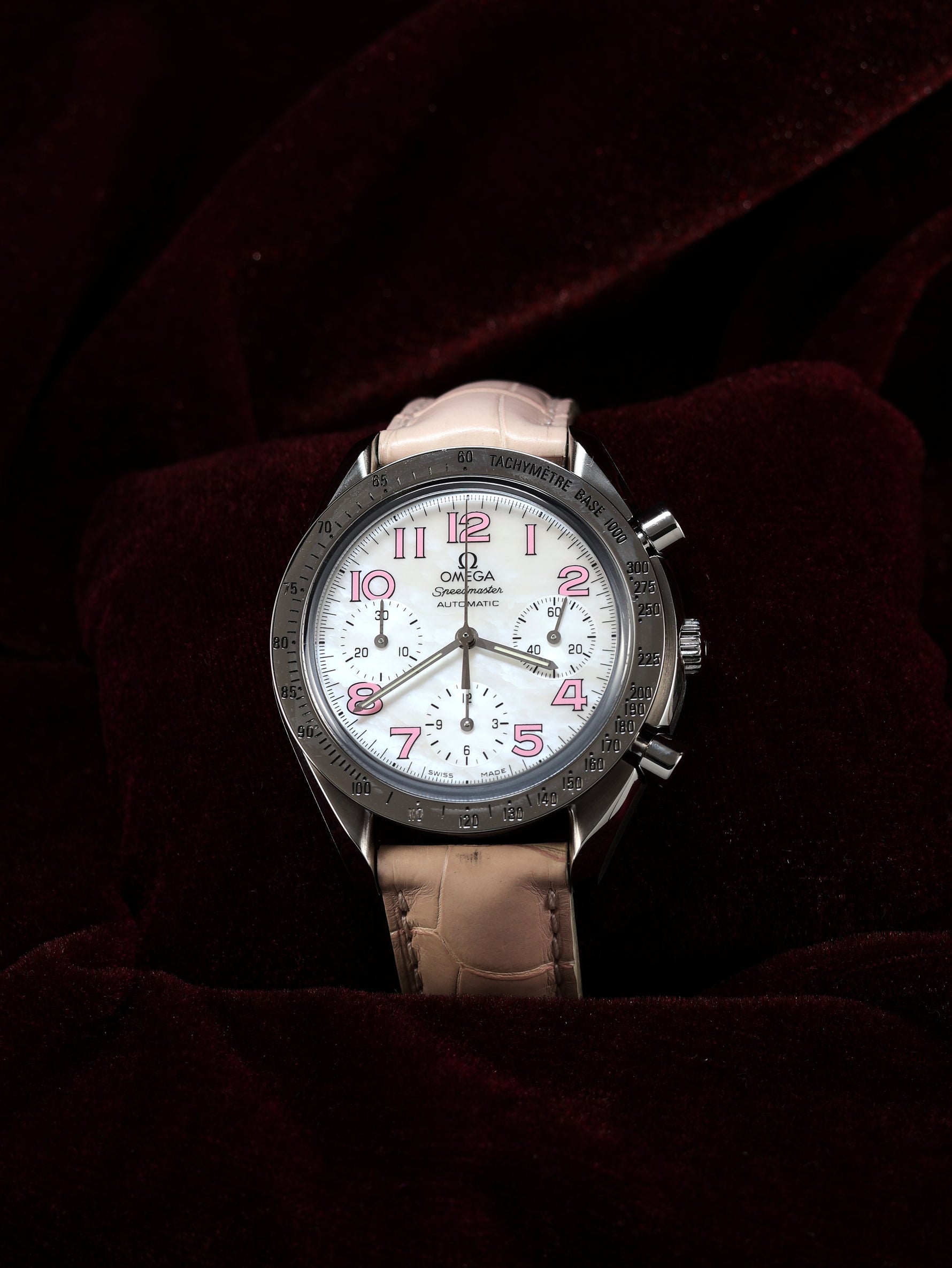 Omega Speedmaster Automatic Chronograph 38mm Ref. 3834.74.34 – angled top view, white mother-of-pearl dial, pink leather strap, dark background