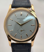 Patek Philippe watch with gold case and black leather strap on a light gray background