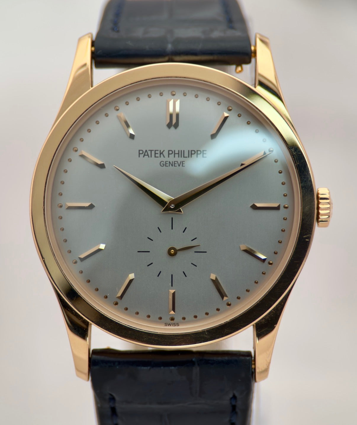 Patek Philippe watch with gold case and black leather strap on a light gray background