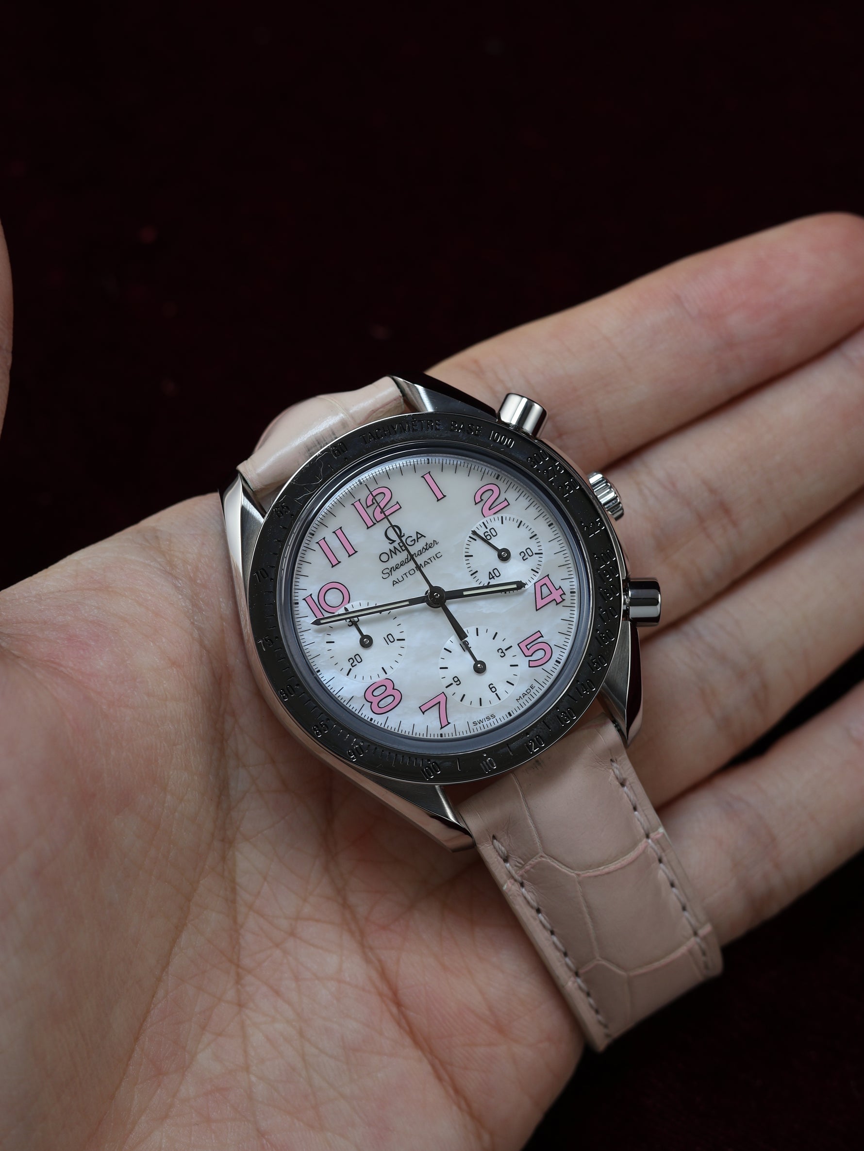Omega Speedmaster Automatic Chronograph 38mm Ref. 3834.74.34 – held in hand, close-up of white mother-of-pearl dial and pink leather strap