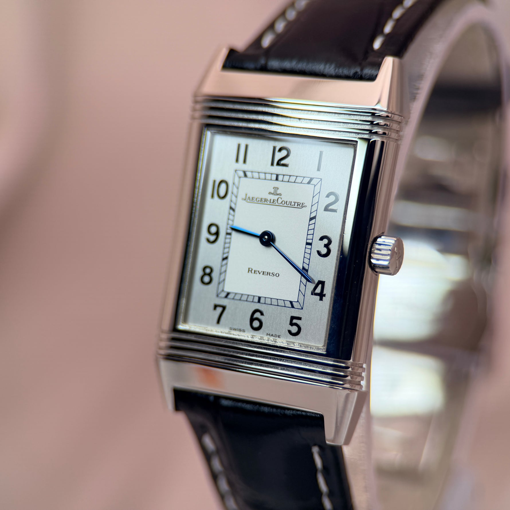 Jaeger-LeCoultre Reverso angled view showing crown and right side of case, white dial with blue steel hands, black leather strap with contrast stitching